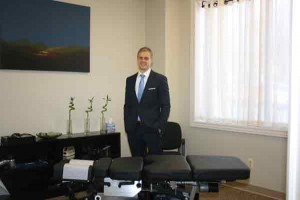 Dr. Nate Keiser stands behind a table inside a room in his Chiropractic & Functional Neurology of Chelsea practice. 