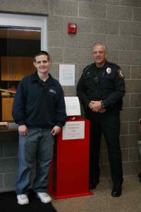 Dispatcher Dan Whitesall and Police Officer Dennis Hall stand next to the Big Red Barrel inside the police sation. 