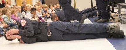 Firefighters demonstrate covering their face and roll showing students what to do if their clothes ever catch fire. 