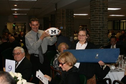 Courtesy photo by Kelly Flaherty. Joey and Lisa from St. Louis Center hold up a Brady Hoke autographed football and Michigan Stadium seat as Jack and Nancy Dunn of Chelsea consider their bids.