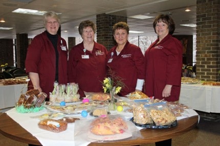 Four of the many Chelsea Community Hospital auxiliary volunteers pose behind one of the many tables of baked goods Tuesday morning. 