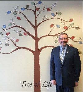 Courtesy photo. Rick Eder stands next to the Tree of Life inside his Farm Bureau Insurance office. 