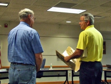 Photo by Crystal Hayduk. Ron Livengood (right), retiring director of operations, shows Steve Olsen, school board president, and board members clippings detailing previous news stories about school district building projects.